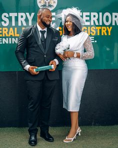 a man and woman standing next to each other in front of a green sign with words on it