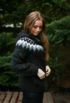 a woman standing in front of some trees wearing a black and white knitted sweater