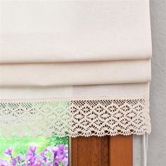 an open window with white curtains and lace on the valance, in front of purple flowers