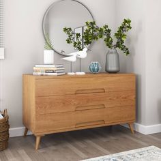 a wooden dresser sitting next to a mirror and vase with plants on top of it