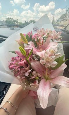 a bouquet of pink flowers sitting in the passenger seat of a car, next to a woman's hand