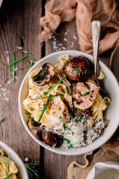 a bowl filled with pasta and mushrooms on top of a wooden table next to other dishes