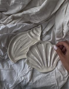 a person is holding a shell shaped dish on a white sheeted bed with sheets