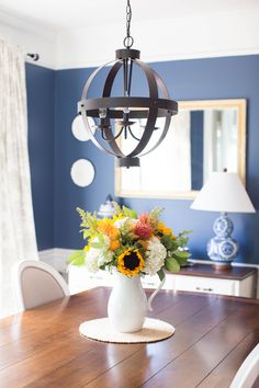 a dining room table with flowers in a vase on it and a chandelier hanging from the ceiling