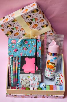 an open gift box with pens, markers and other items in it on a pink background