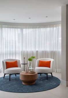 a living room with two white chairs and a round coffee table in front of the window