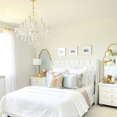 a white bedroom with chandelier, bed and dresser