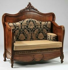 an ornate wooden couch with pillows on it's back and arm rests against the wall