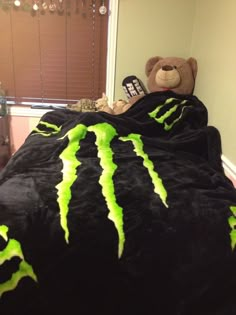 a teddy bear sitting on top of a bed covered in a black and green monster blanket