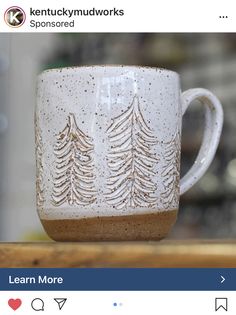 a coffee cup with trees on it sitting on a wooden table next to an instagram post