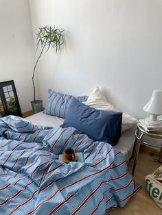 a bed with blue and red striped sheets in a room next to a potted plant