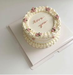 a white cake sitting on top of a box covered in frosting and pink flowers