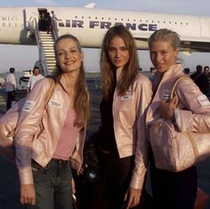 three girls in pink jackets standing next to an air france plane on the tarmac