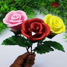 someone is holding three fake roses in their hand, one pink and one yellow with green leaves