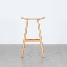 a wooden stool sitting on top of a cement floor in front of a white wall