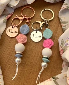 three keychains with name charms on them sitting on a table next to a scarf