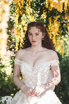 a woman in a wedding dress standing under a tree with yellow flowers on the branches