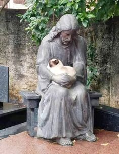 a statue holding a cat sitting on top of a cement bench next to a tree