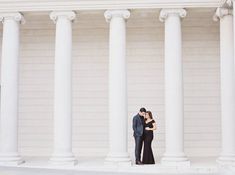 an engaged couple standing in front of some white pillars