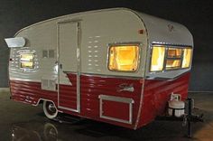 an old camper trailer is parked in a garage with its lights on and the door open