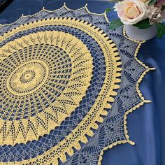 a crocheted doily on a blue table cloth with flowers in the background