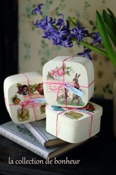 three small boxes are sitting on a table with flowers in the vase and one has a ribbon tied around it