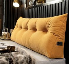 a bed with a yellow pillow on top of it next to a mirror and lamp