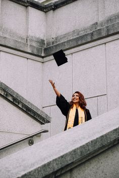 a woman wearing a graduation cap and gown waves to someone from the top of some stairs