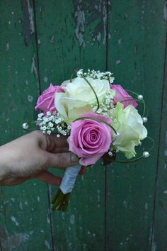 a person holding a bouquet of pink and white flowers in their hand on a wooden background