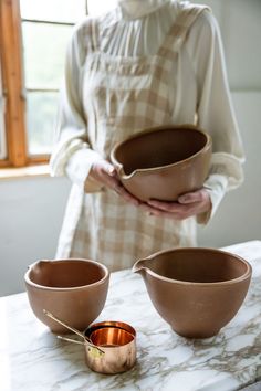 a woman holding three bowls on top of a marble counter next to an empty bowl