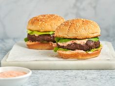 two hamburgers sitting on top of a white plate next to a bowl of dipping sauce