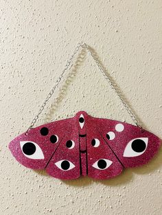 a pink and black butterfly hanging from a chain on a wall with eyes painted on it