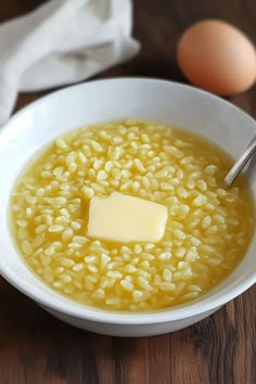 a white bowl filled with soup next to an egg on top of a wooden table