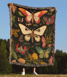 a woman is standing in front of a blanket with butterflies on it and trees behind her