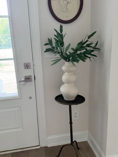 a white vase sitting on top of a black table next to a door with a plant in it