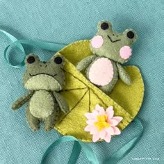 two small stuffed animals sitting on top of a green cloth covered object with a flower