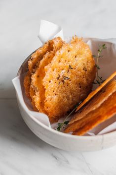 a white bowl filled with fried food on top of a marble countertop next to bread sticks