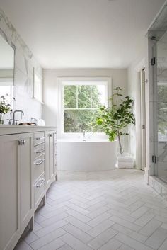 a white bathroom with a large window and marble tile flooring, along with a plant in the bathtub