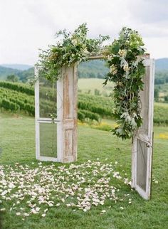 an outdoor ceremony setup with flowers and greenery on the grass in front of two open doors