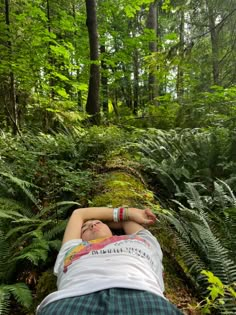 a person laying down in the woods with their head on his hands and eyes closed