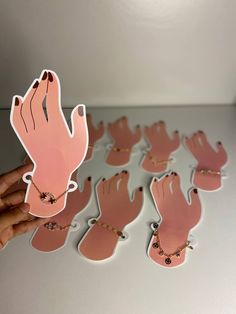 a hand holding a pink sticker next to several pairs of hands on a white surface