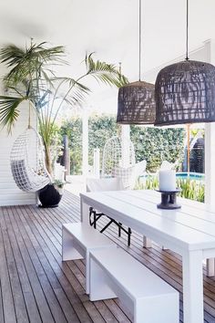 a white table sitting on top of a wooden floor next to a palm tree and hanging chairs