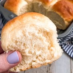 a person holding a piece of bread in front of a pan with rolls on it