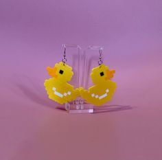 a pair of yellow rubber ducky earrings hanging from acrylic hooks on a purple background