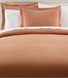 the bed is made with peach colored linens and white pillow cases on top of it