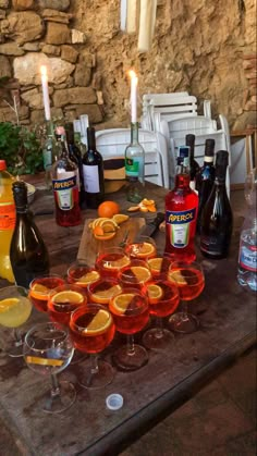 there are many glasses on the table with oranges and bottles in front of them