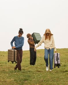 three people walking in the grass with suitcases on their back and one carrying a box