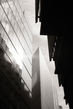 black and white photograph of tall buildings with the sun shining through them in the background