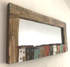 a wooden frame mirror hanging on the wall with houses painted on it's sides