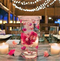 a vase filled with pink flowers and pearls on top of a table next to candles